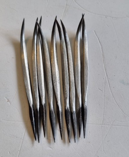 Nine metal diamond curved awls with curved silver bodies and dark pointed tips, arranged vertically on a light gray textured surface.