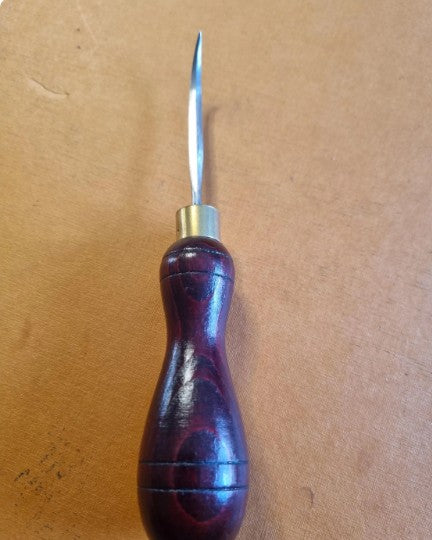 A hand tool with a polished dark reddish-brown wooden handle and a sharp silver metal diamond awl blade, resting on a brown textured surface.