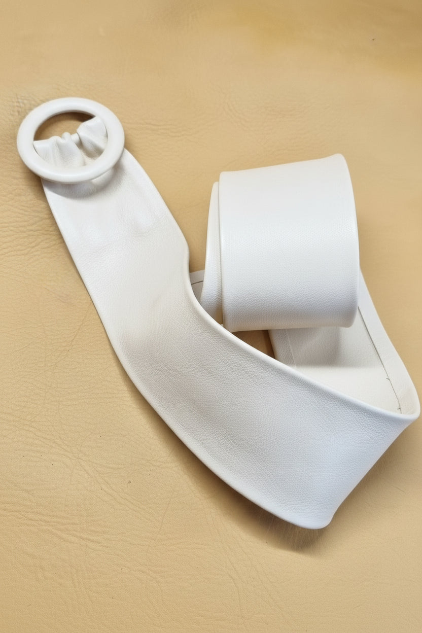 A white cinch leather belt with a wide strap and a circular leather covered buckle, displayed on a textured tan leather background.
