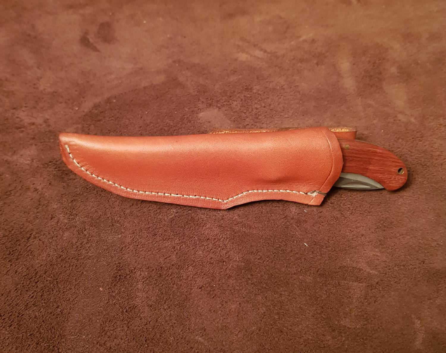 A brown leather knife sheath designed for a 6-inch friction knife, with stitching and a flap closure, placed on a textured background.