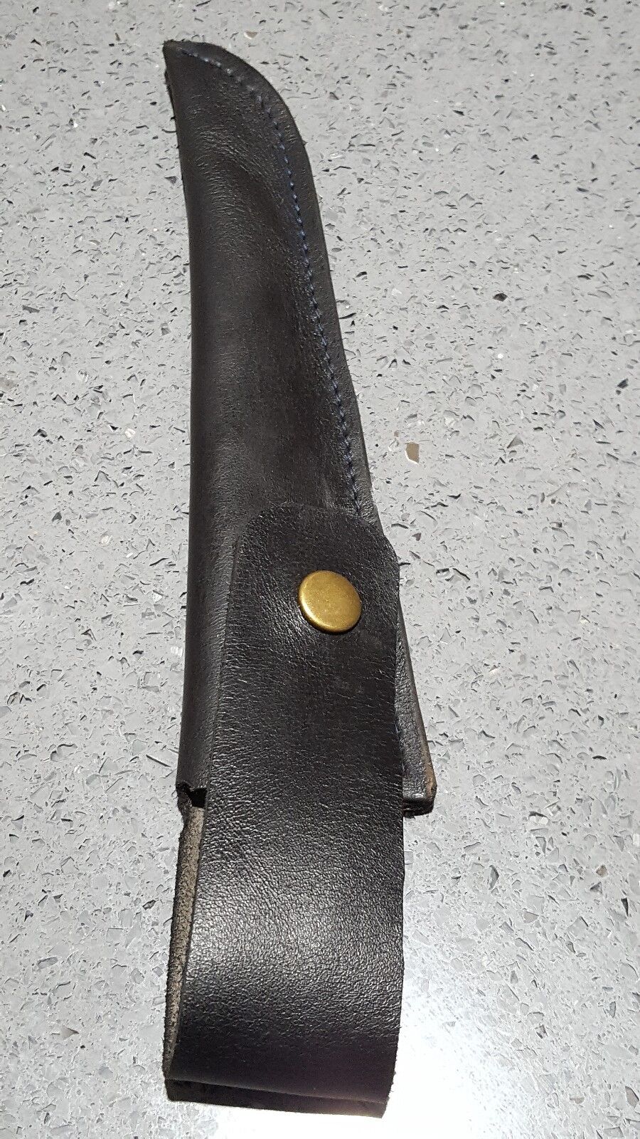 Close view of black leather filleting knife with snap closure on a grainy background