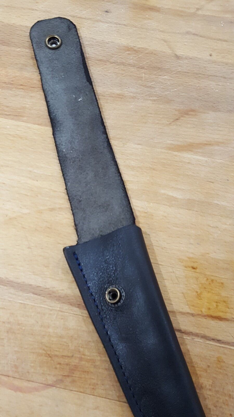 Close view of black leather filleting knife showing open closure loop  a wooden background