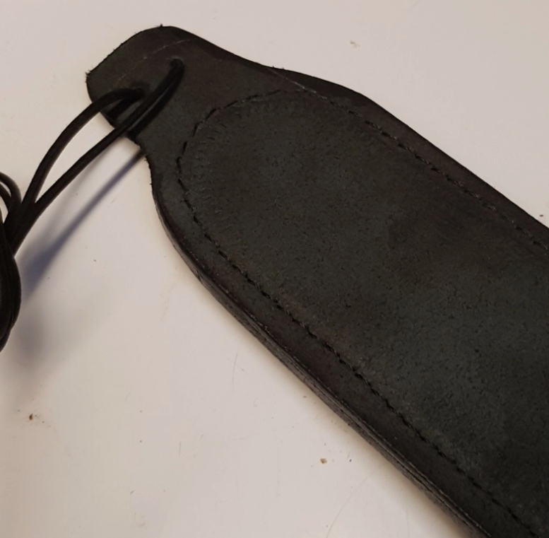 A close-up of a back of black leather sheath with a looped leather lace and visible stitching, photographed on a plain light background.