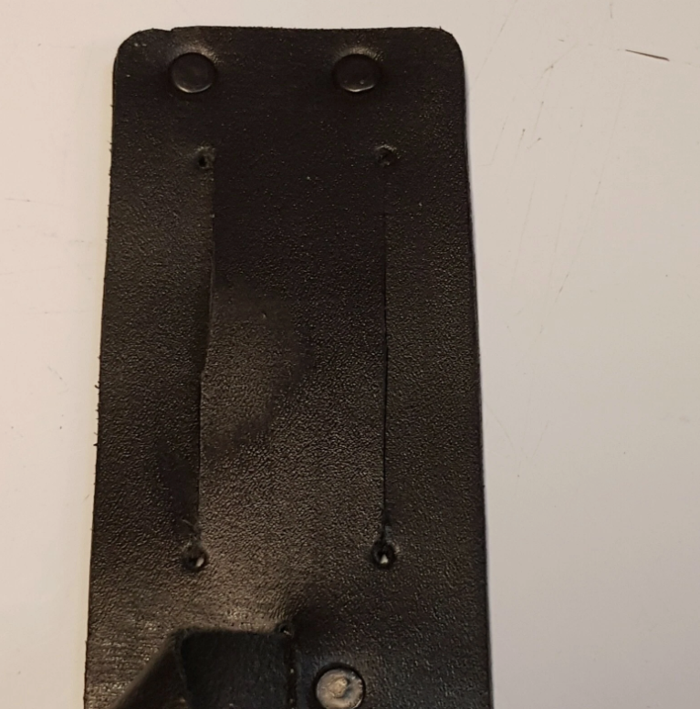 A close-up of a black leather sheath belt slot with pre-drilled holes, shown against a plain off-white background.