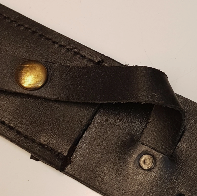 Close-up of a black leather strap with a brass snap button and a small metal rivet on a plain light background.