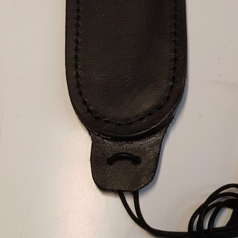 A close-up of a black leather sheath toe with visible stitching and a looped leather lace end, photographed on a plain light background.