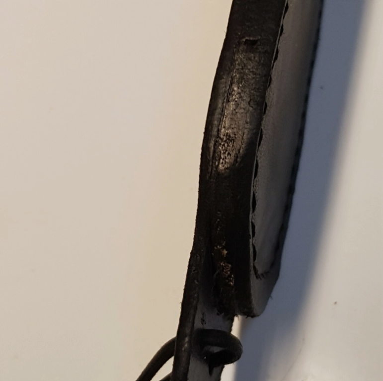 A close-up of a black leather commando sheath welt edge with visible wax finish and a small loop at the bottom, photographed against a plain off-white background.