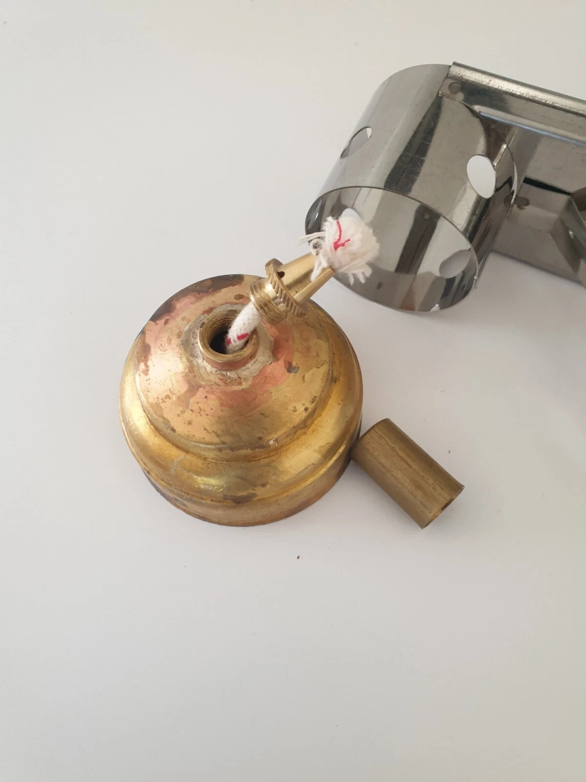 A brass lamp base with a white wick set against chrome finished metal stand, displayed on a plain white background