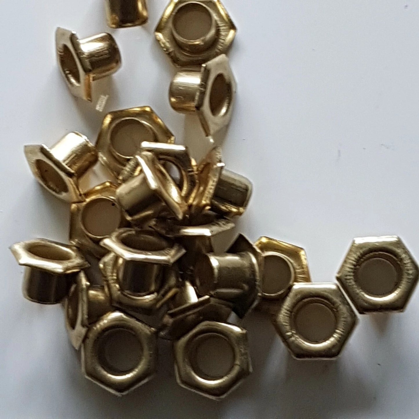 A pile of small metallic gold hexagonal ring-shaped beads or spacer beads scattered on a plain white background.