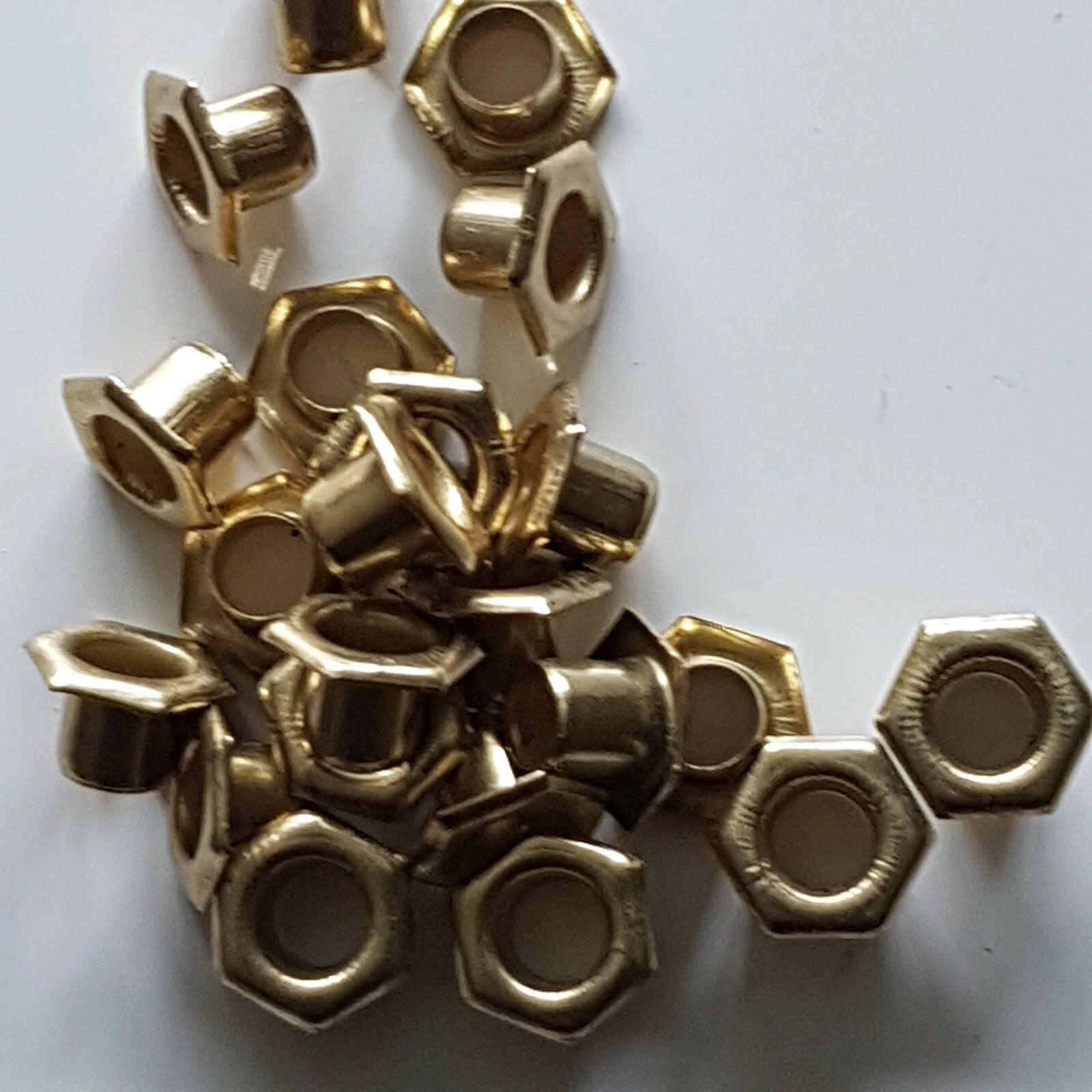 A pile of small metallic gold hexagonal ring-shaped beads or spacer beads scattered on a plain white background.