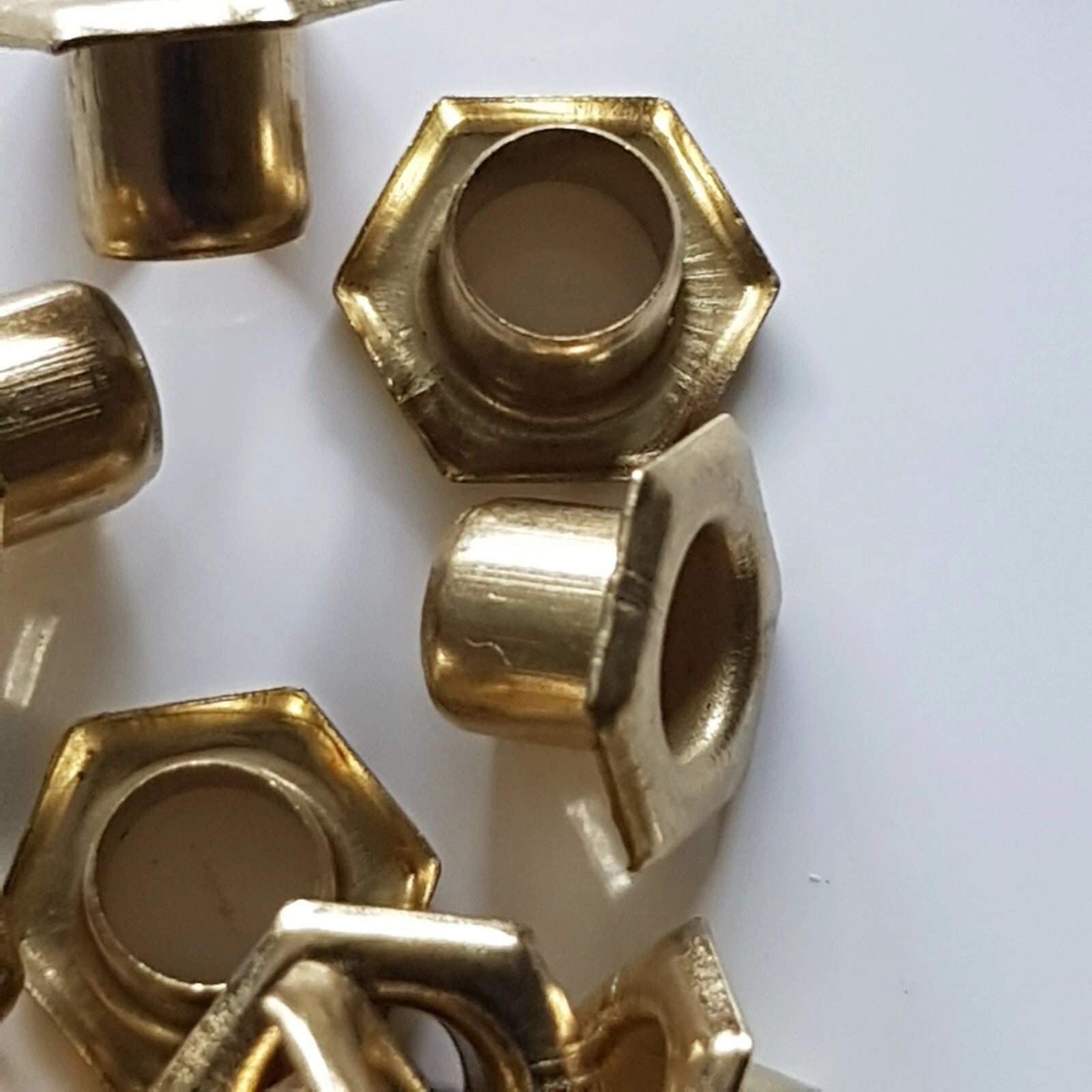Several brass hexagonal sleeve nuts with hollow centers, displayed on a plain white surface.