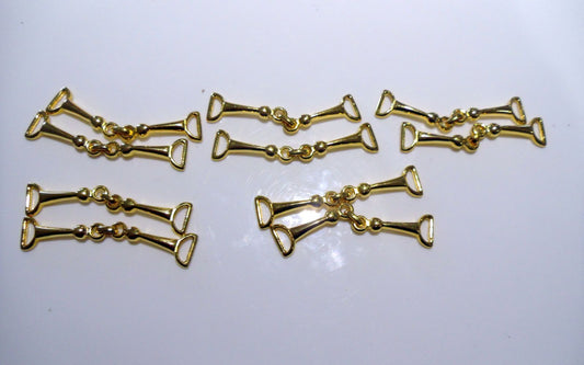 A collection of eight gold-colored metal moccasin trims arranged in two rows on a light background.