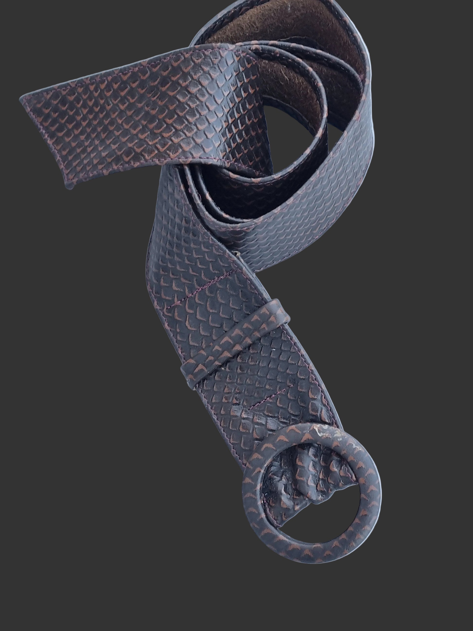 A dark brown rattle snakeskin embossed leather belt. Large circular leather covered buckle, displayed on a light blue background.