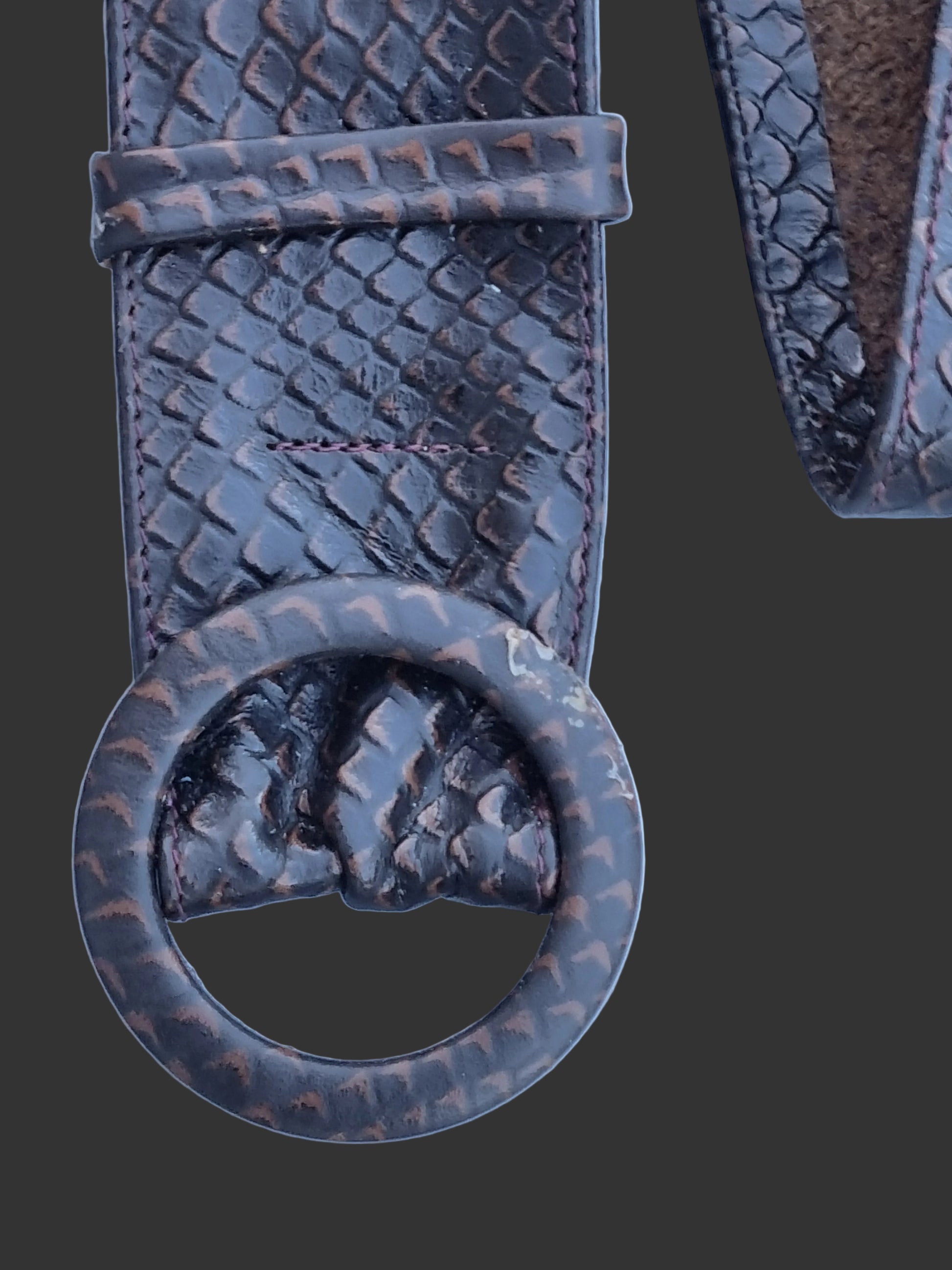 A close up view of dark brown rattle snakeskin embossed leather belt showing matching leather covered buckle, displayed on a light blue background.