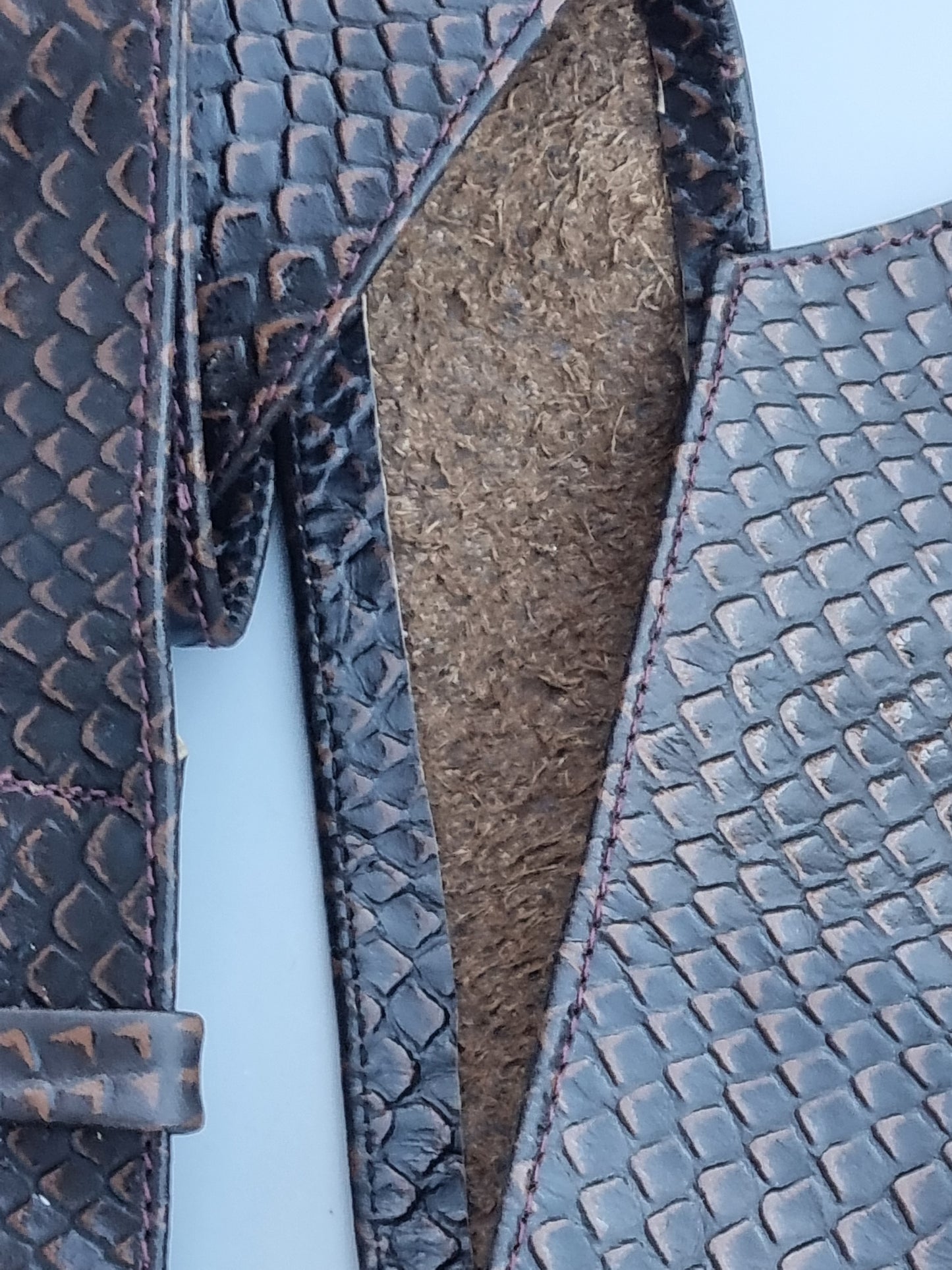 Close-up of a dark brown rattle snake embossed  leather belt and back of the belt. Shown against a light blue background.