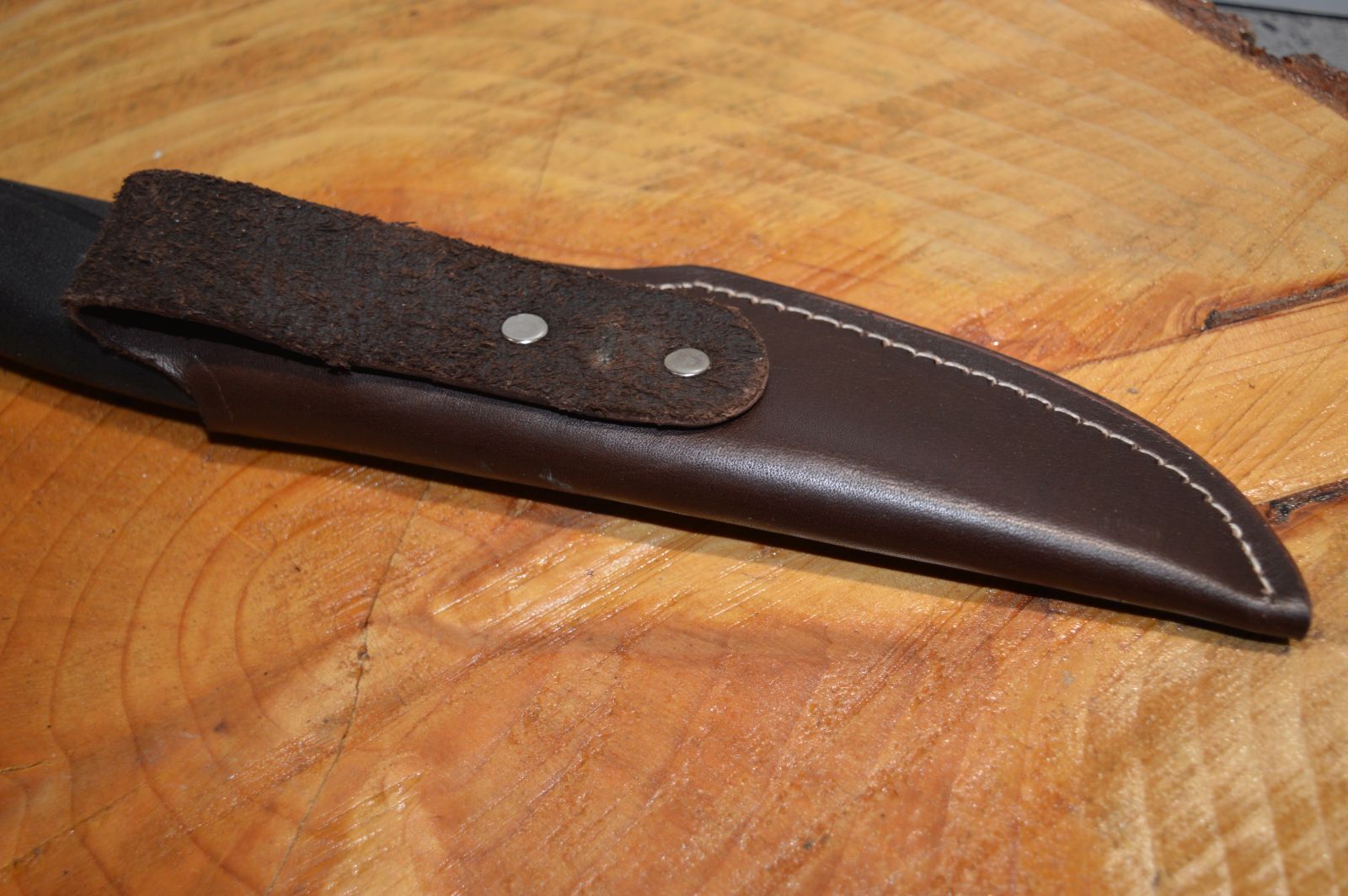 Close view of back of the black leather sheath for a Morakniv 860 type knife showing belt loop on wooden background 