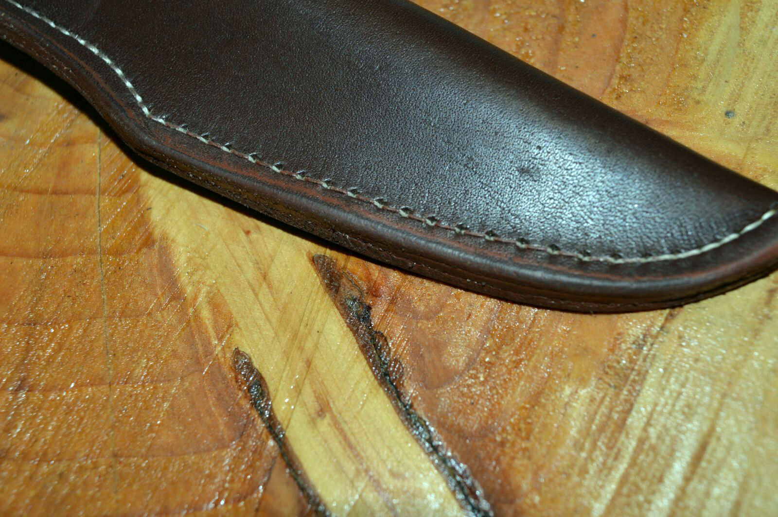 Close view of black leather sheath for a Morakniv 860 type knife showing detailed stitching on wooden background 