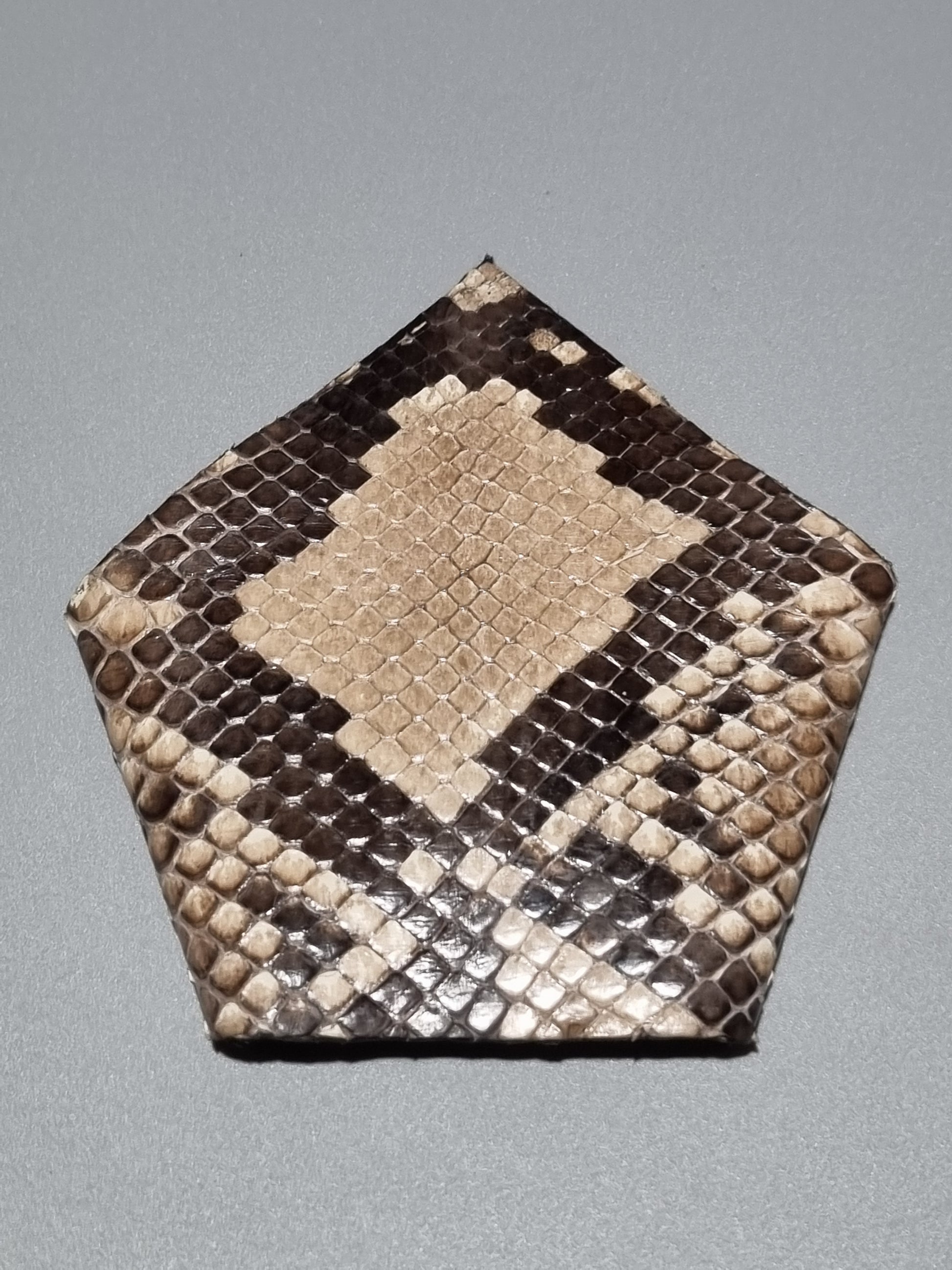 One point suit pocket made from real python snakeskin showing natural patterns of brown, beige, and black large scales, displayed on a neutral gray background.