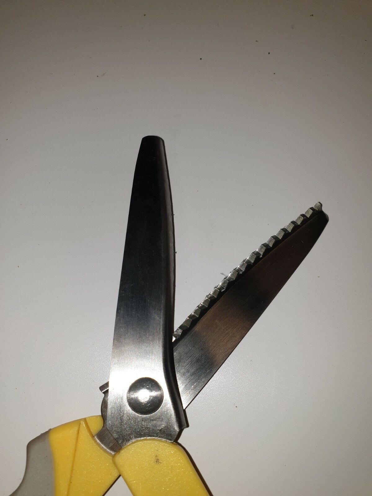 Close view cutting blades of  pinking gimping scissors with yellow and grey plastic handles and a stainless steel blade, designed for leathercraft work.