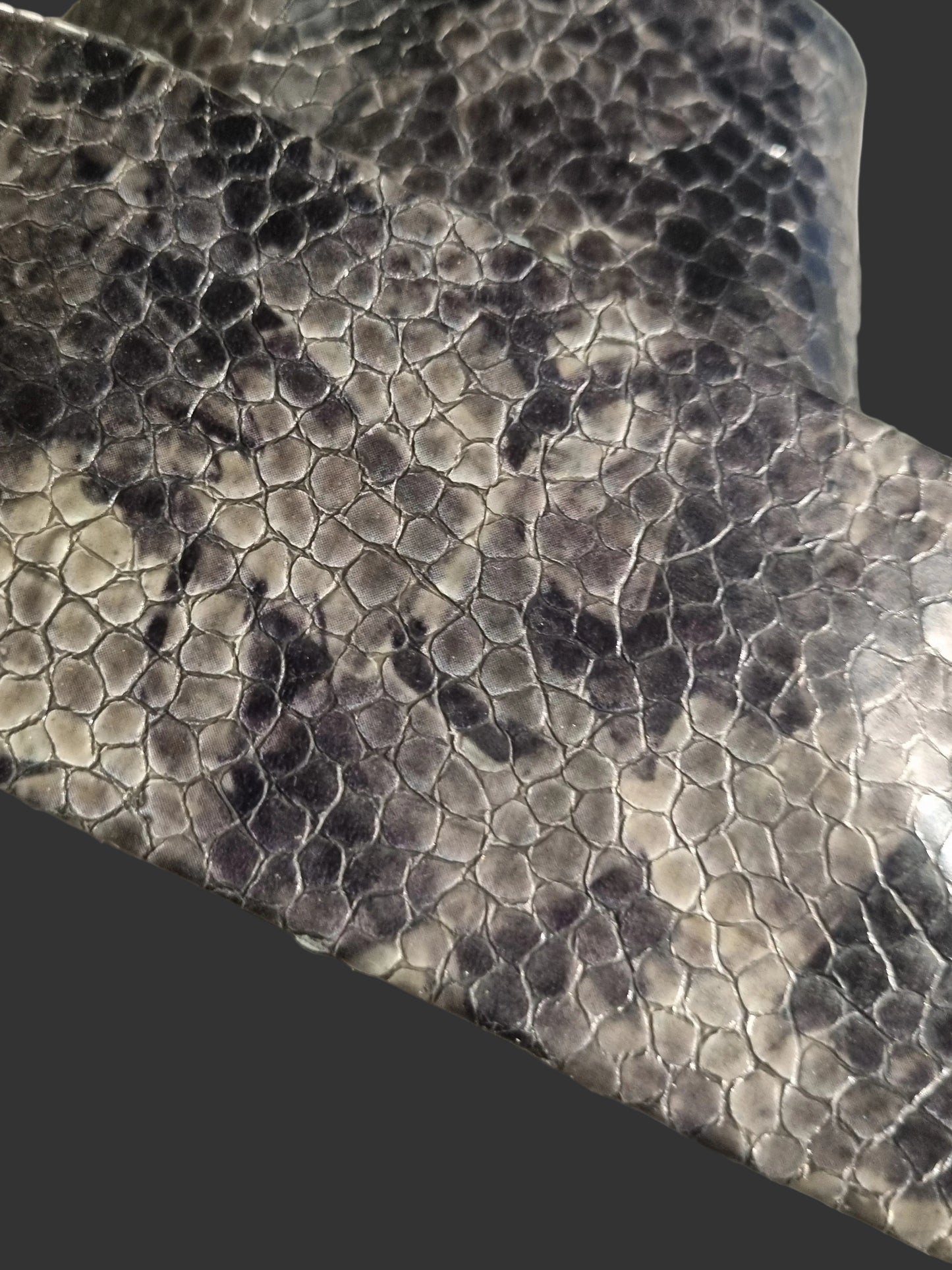 Close-up of a snakeskin-patterned leather belt showing detail of scales and colour with gloss finish, draped diagonally across a light surface.