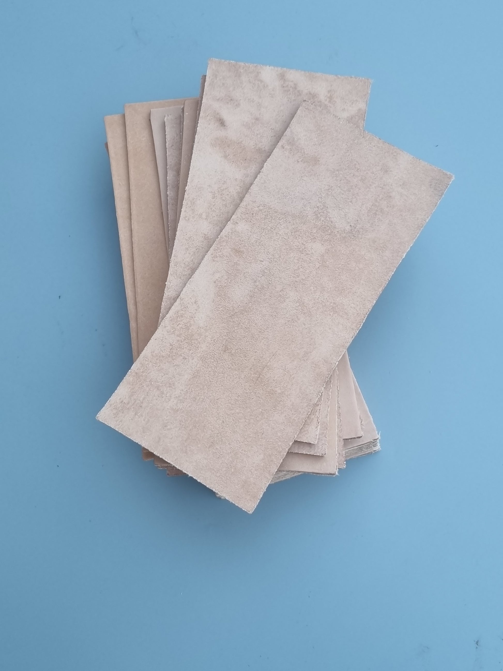 A stack of rectangular leather sheets, arranged diagonally on a solid light blue background.