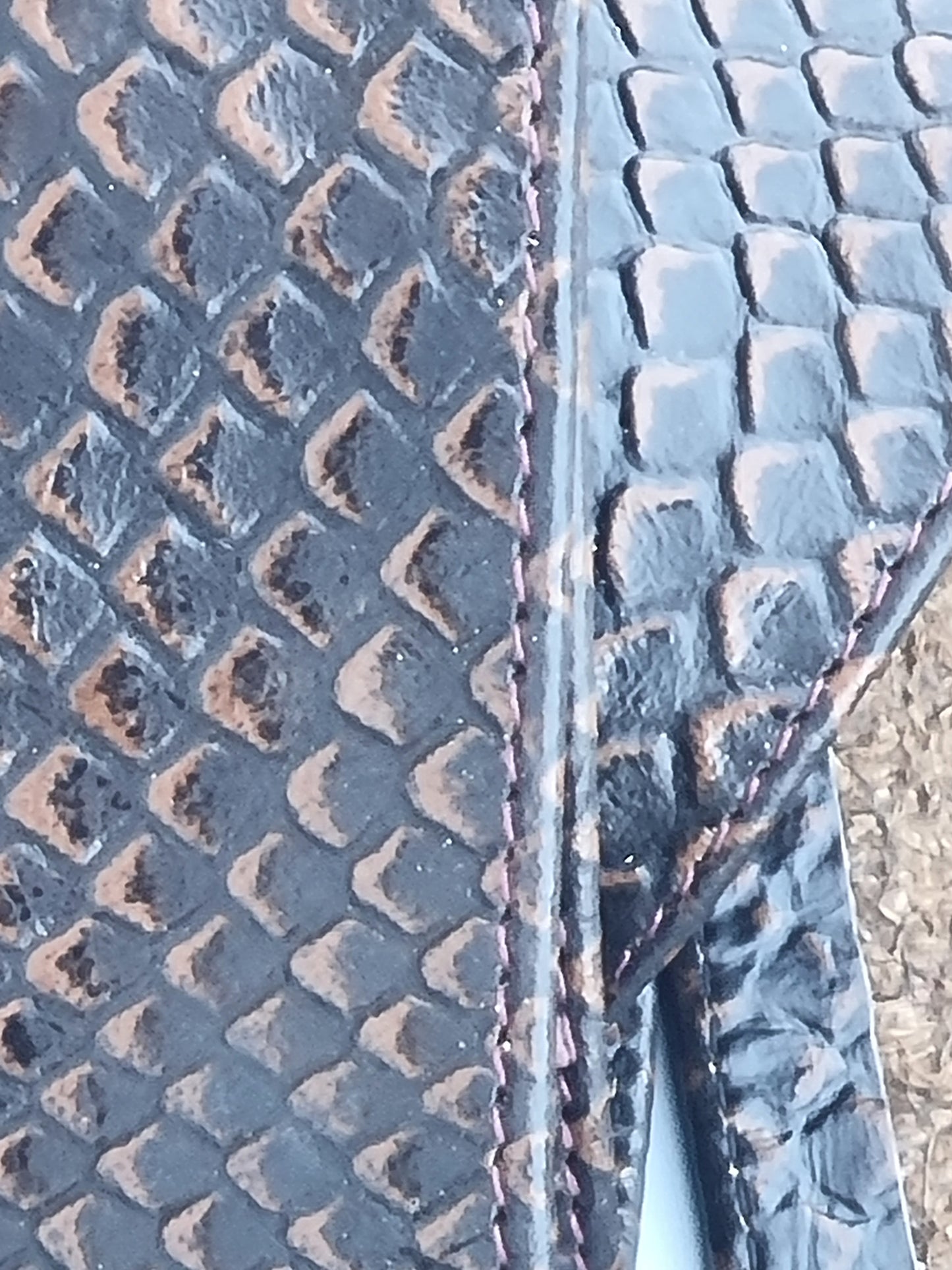 Close-up of a dark textured material with a raised scale-like pattern and visible stitching along a seam.