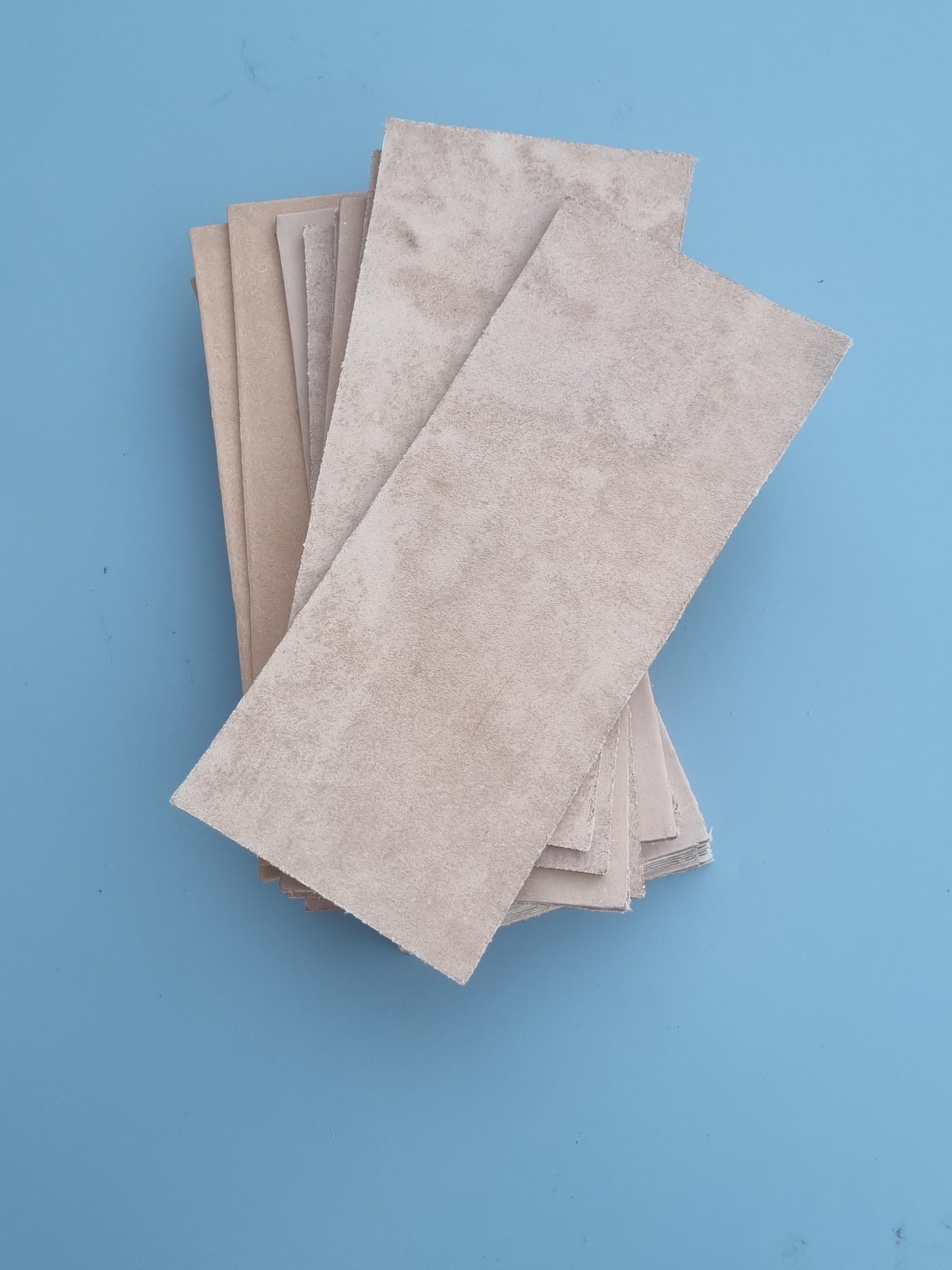 A stack of rectangular beige leather  sheets, arranged diagonally on a solid blue background.