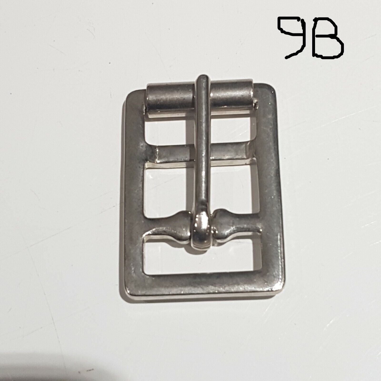Single metal saddlery buckle with a chrome finish on a white background, labelled 9B 