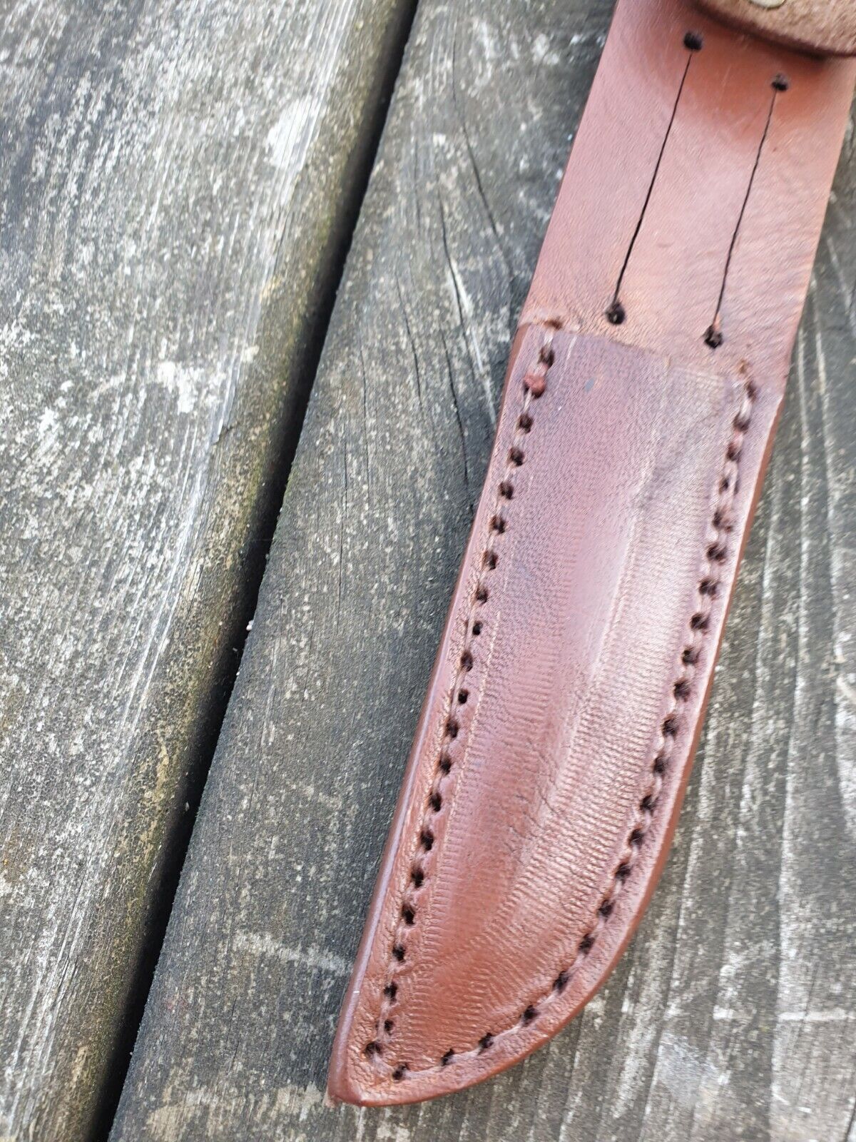 Close view of Scout knife sheath in brown colour showing stitching and belt slot on a wooden background