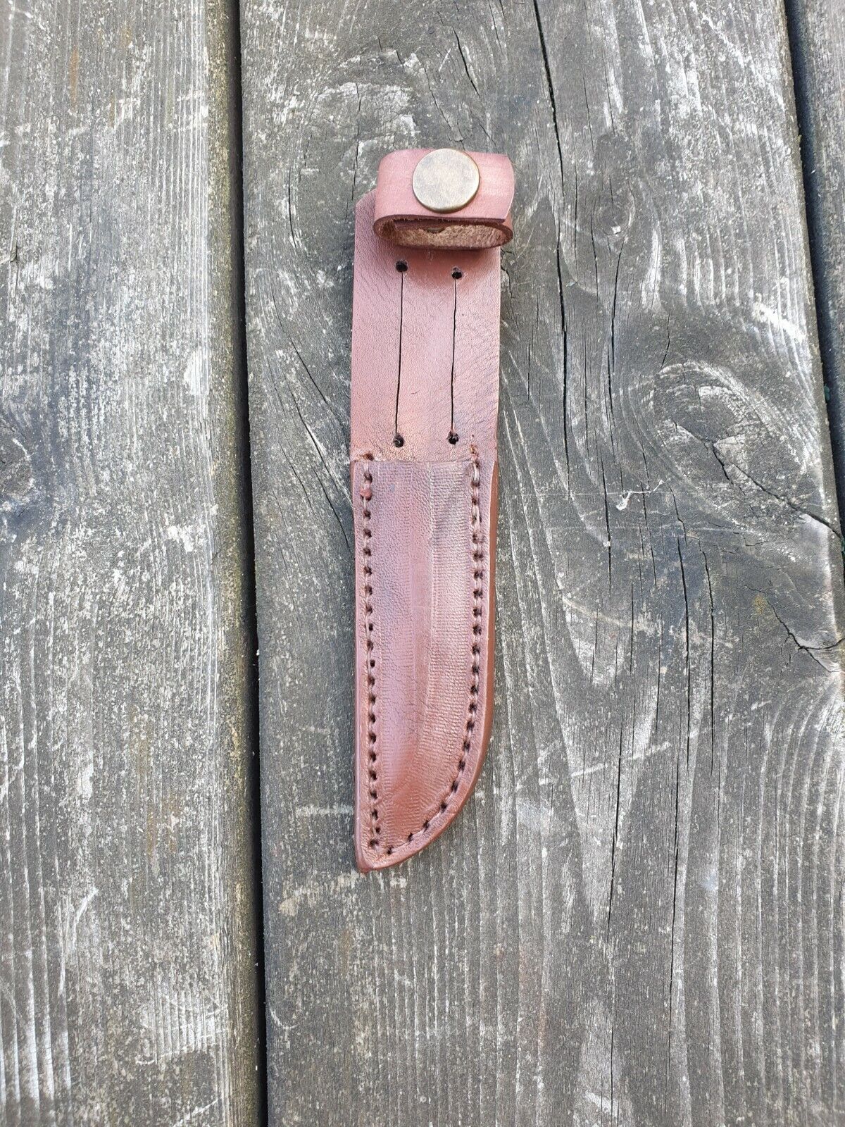 Scout knife sheath in brown colour showing stitching and snap loop on a wooden background