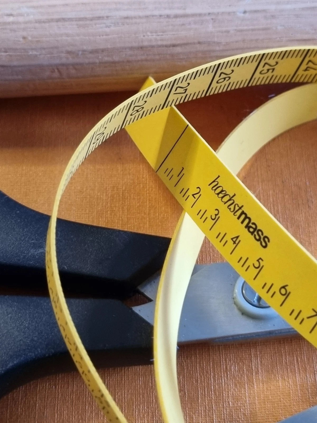 A close-up of a shoemakers yellow measuring tape with black printed markings and the brand name 'horchtmass' visible, resting on a wooden surface next to a black-handled tool.