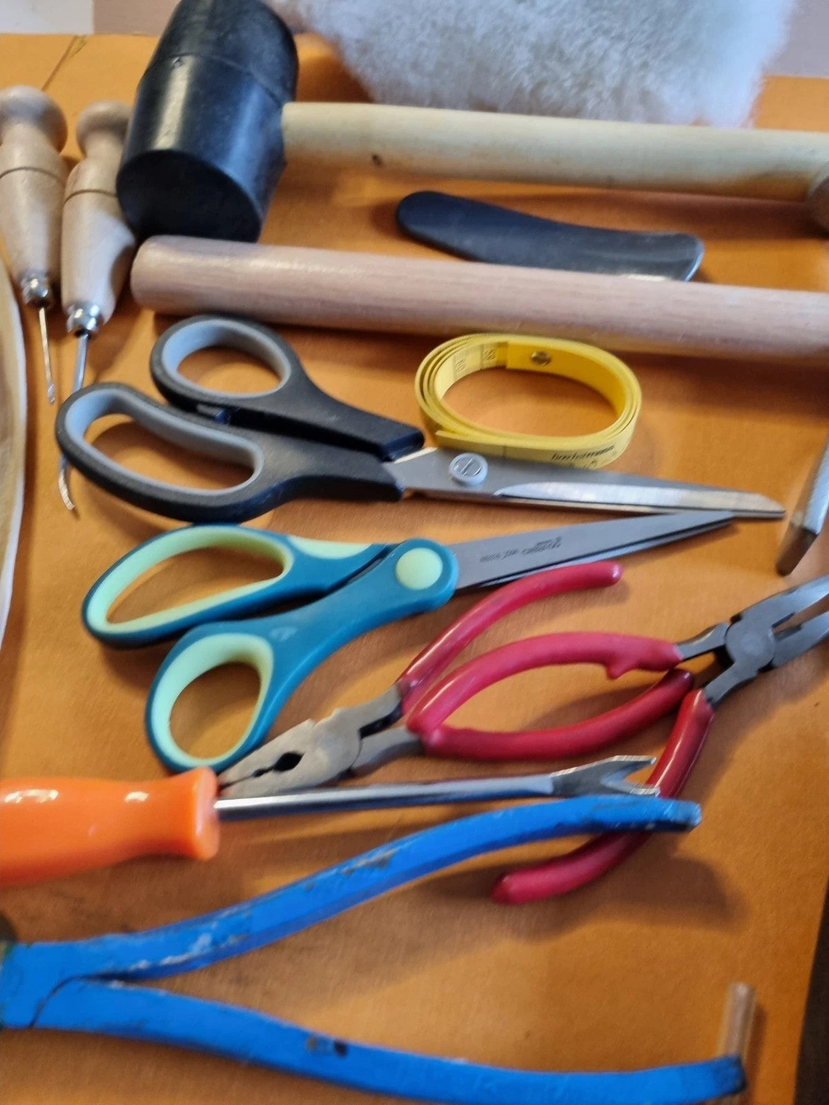 A collection of hand tools with colorful handles, including scissors, pliers, a hammer, and a wooden mallet, arranged on a wooden surface.