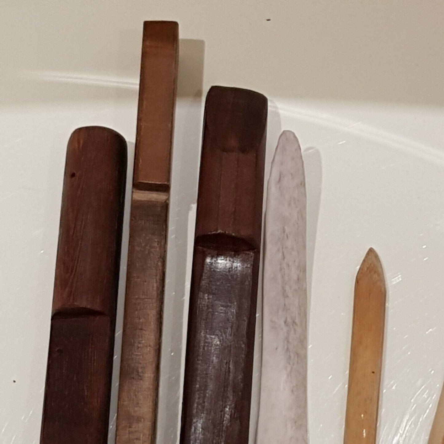 Close view of 5 wooden burnishing tools along with cow bones displayed on white back ground