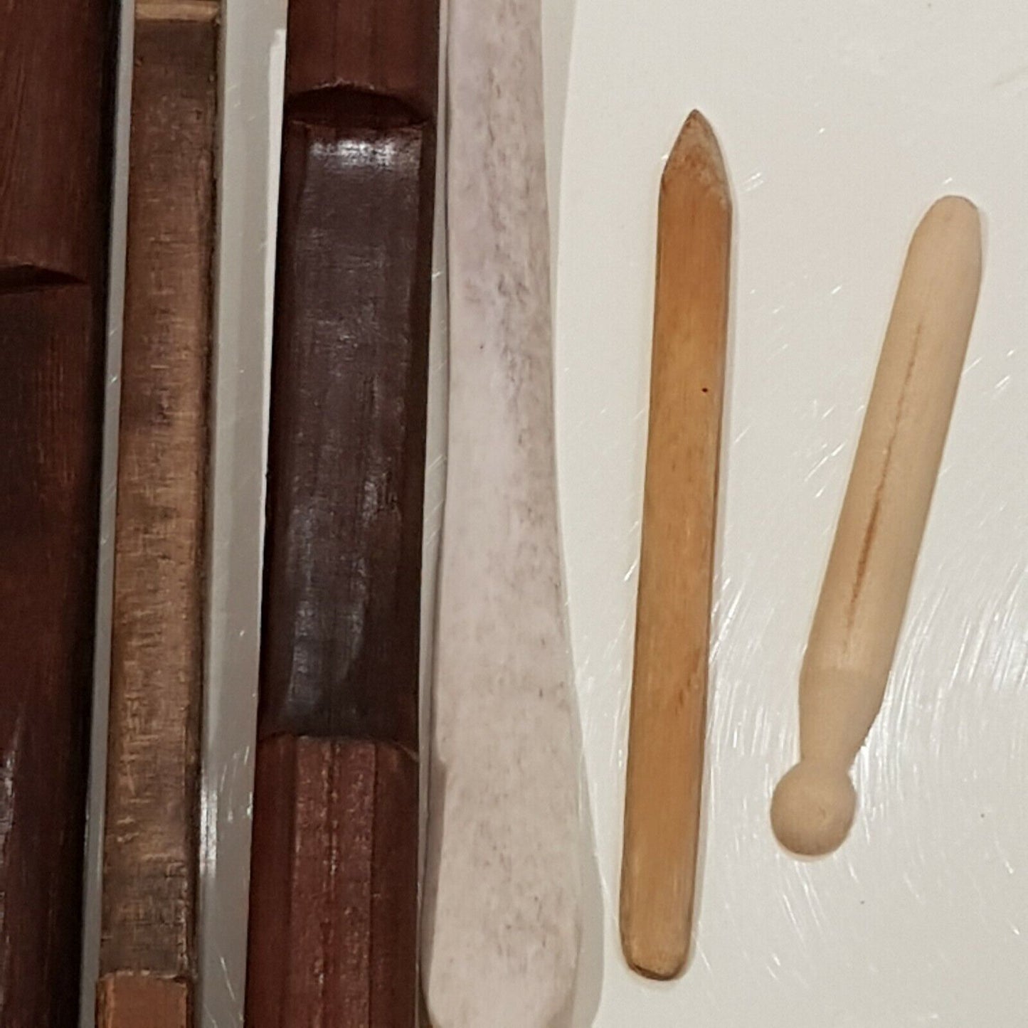 Close view of 4 wooden burnishing tools along with cow bone displayed on white back ground