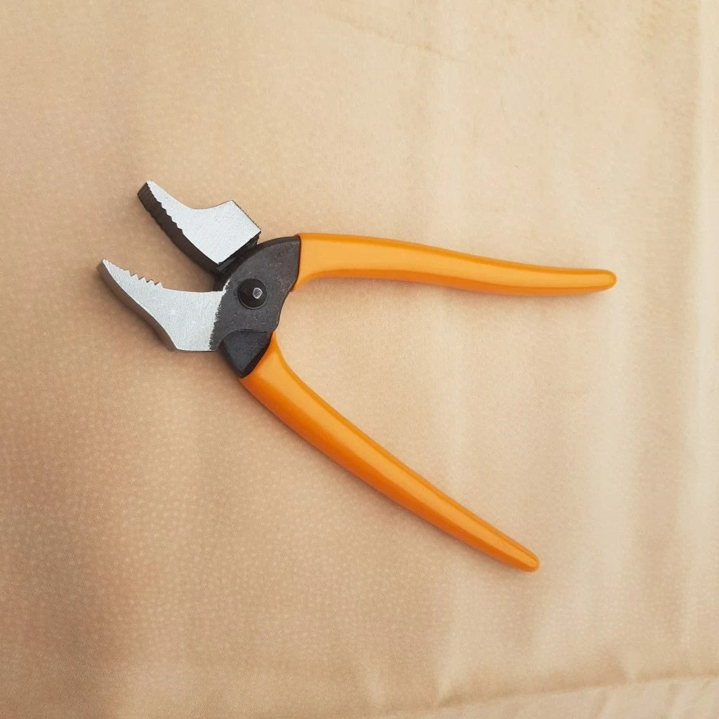Open jaw curved nose lasting pliers with silver metal jaws and a black pivot section, placed on a beige textured surface.