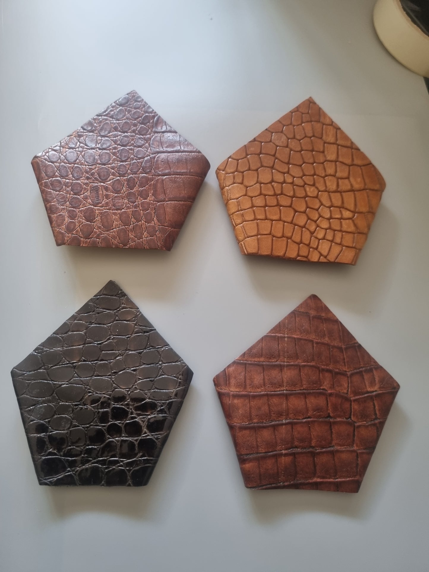 Four crocodile print leather suit square pockets accessories arranged in a 2x2 grid on a light grey surface. The top-left is tan, the top-right is medium brown, the bottom-left is reddish brown, and the bottom-right is dark charcoal grey.