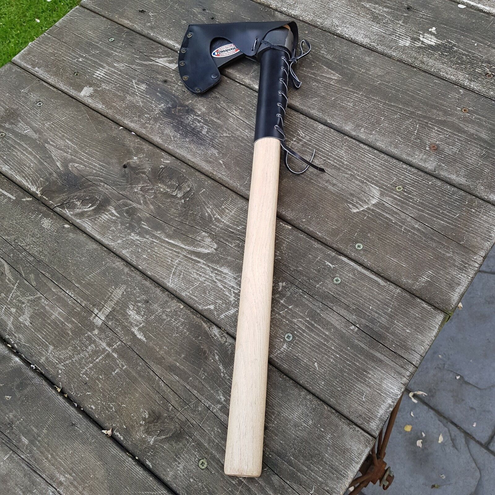 Tomahawk axe with wooden handle leather protector and axe head leather sheath displayed on a wooden surface.