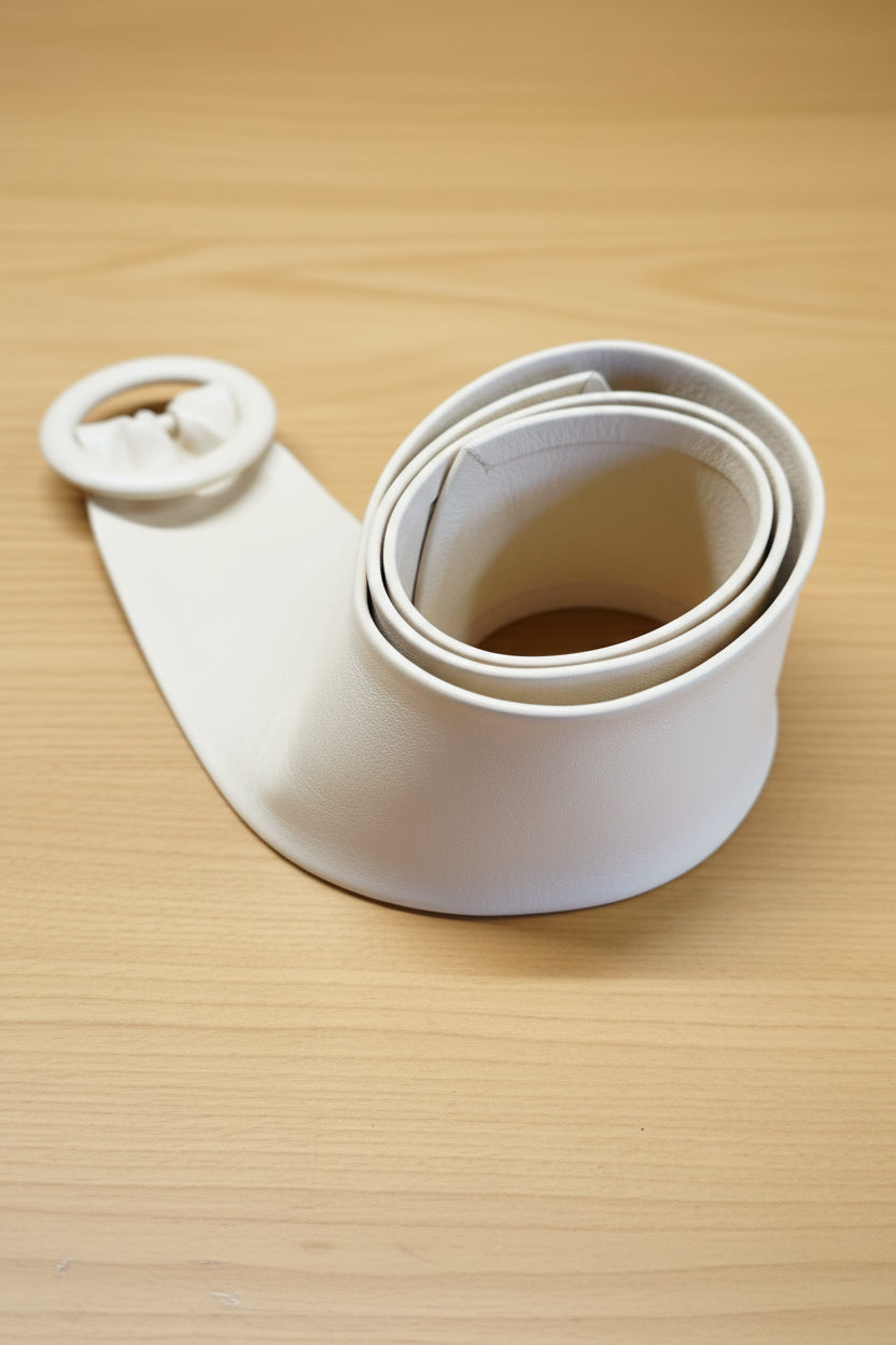 Close of the white women cinch leather belt with a large circular leather covered buckle, coiled on a tan textured leather background.