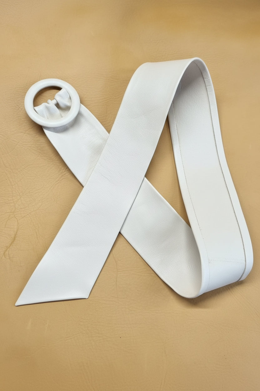 Handmade white leather cinch belt with matching leather covered buckle, arranged in an X-shape on a textured tan leather background.