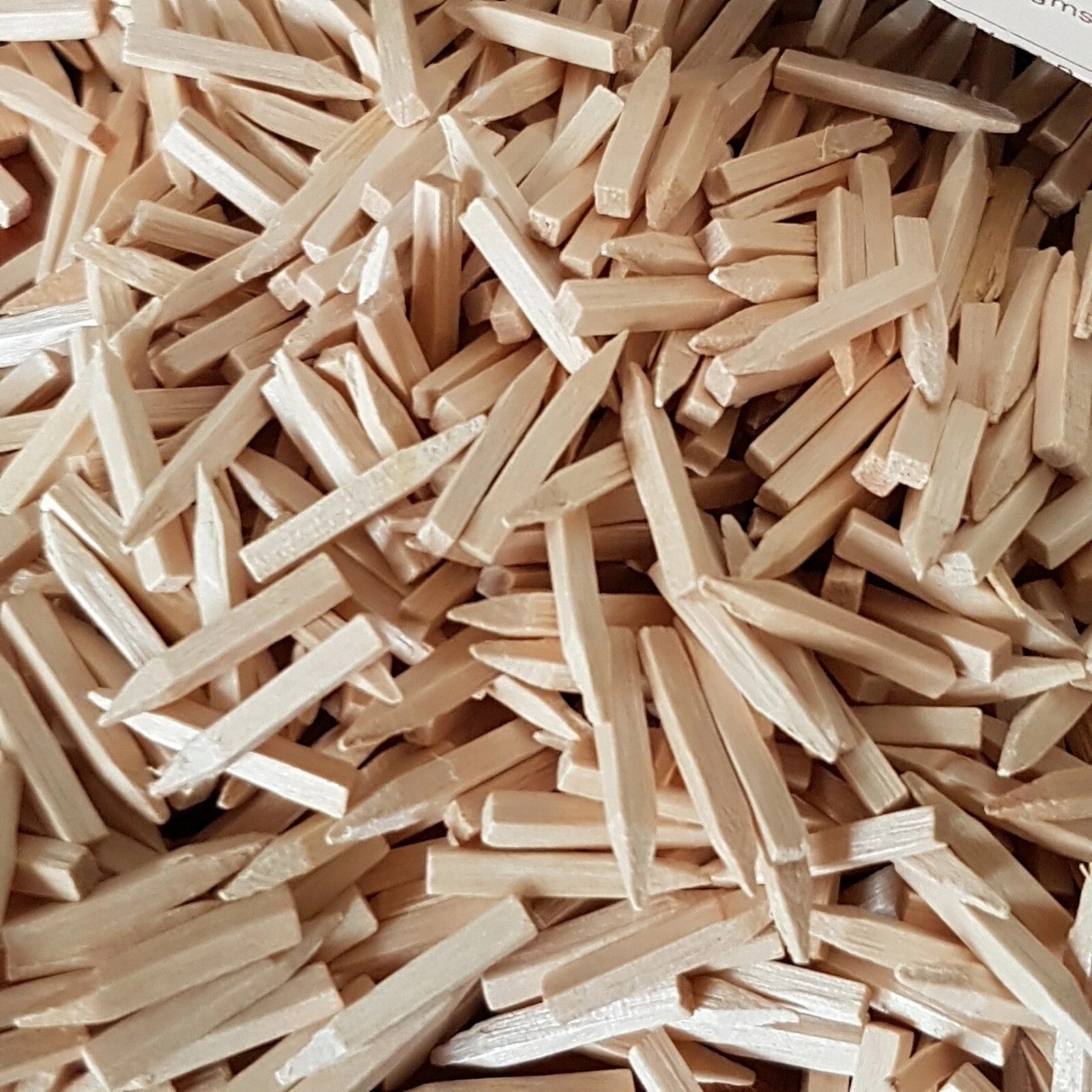 A close-up pile of light natural wood pegs or nails filling the frame, with no person, animal, or real environment visible.