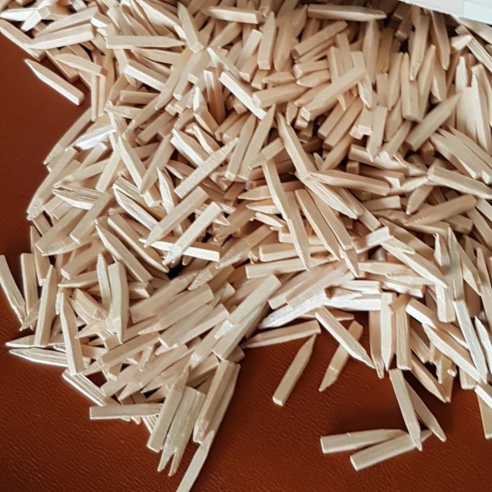 A pile of small, light beige rectangular wooden nails scattered on a brown textured surface.